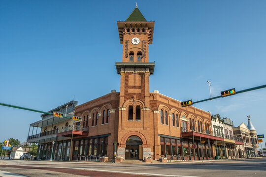 Red Brick Building With Tall Clock Tower and Shops Along Sidewalk in Downtown Grapevine, Texas With Blue Sky