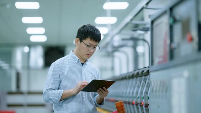Engineer in factory workshop holding tablet to inspect equipment on production line