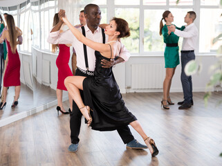 Fototapeta premium Dynamic middle-aged male and female attendees of dancing courses doing waltz in group