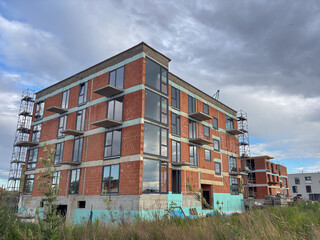 a brick apartment building under construction with scaffolding against a cloudy sky, concept of real estate development, urban expansion, and modern architecture for construction companies