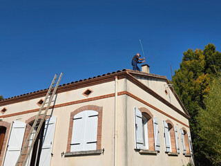 A worker stands on a roof to fix a chimney
