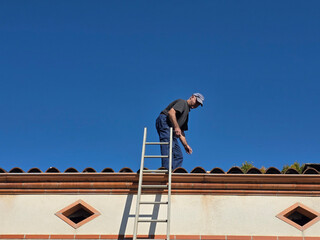 Man repairs the roof while standing on a ladder