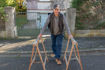 Man carries wooden sawhorses onto the street near a house