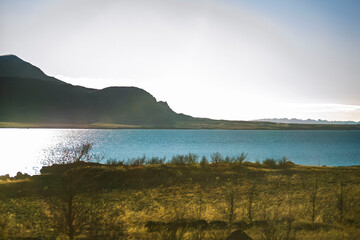 Bright Shimmering Sunlight Reflecting on Fjord Water with Mountain Silhouettes and Golden Tundra