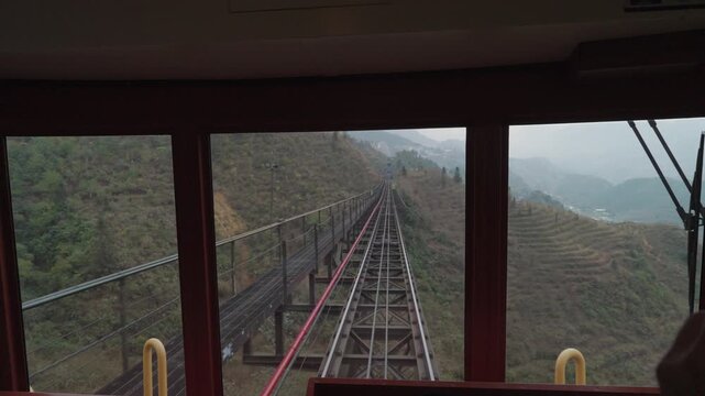 View from inside the Muong Hoa funicular in Sapa, Vietnam, showing railway tracks cutting through lush green hills and misty mountain forest, creating a calm and atmospheric travel scene.