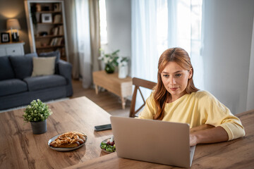 Fototapeta premium Woman working on laptop while eating at home