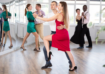 Fototapeta premium Woman in elegant evening dress dances incendiary tango with male partner during choreography lesson. Group training and rehearsal, preparation for competitions
