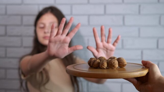 Nut allergy. Unhappy teenage girl showing a stop gesture with her hands, refusing a plate of walnuts due to a potential food allergy, intolerance, or dietary restriction for a healthy lifestyle