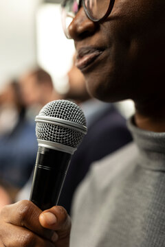 Close up of black woman attendee asking questions on microphone during panel discussion, engaging in debate at international summit. Business conference with presentation on stage.