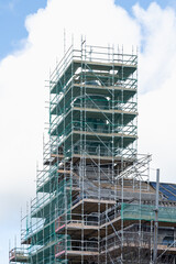 Fototapeta premium Multi-story building under construction covered with metal scaffolding. Urban construction site with safety structures, renovation works and architectural framework against a cloudy sky. 