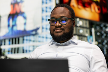 Obraz premium Black man siting on a bench in urban park scrolling through laptop and navigating website, casual street style and attitude highlighted by sunlight and modern city life scenery.