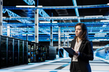 Fototapeta premium Data center manager using tablet, managing server virtualization. System administrator using device in server room, doing upgrades sustaining long term infrastructure reliability