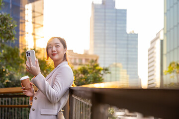 Fototapeta premium Luxury young Asian CEO woman entrepreneur using mobile phone while walking in the urban skyscraper street modern office downtown on background for business communication and urban lifestyle