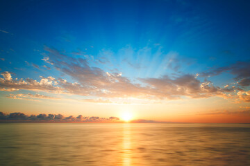 Fototapeta premium Bright beautiful orange sunset on the beach and by the sea, smooth sea, sunny path in the sea, sun on the sea horizon, sun rays in the blue sky - Vintage filter