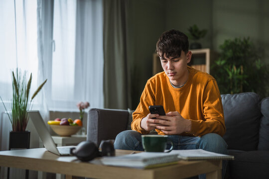Teenage boy using smart phone, distracted from studying at home