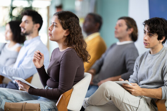 Young woman in multinational group listens to lecture and taking notes in lecture hall