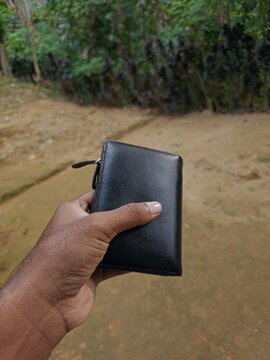 Close up of a person holding a minimalist black leather wallet, personal finance and savings concept

