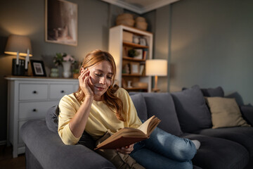 Obraz premium Woman relaxing at home reading a book on couch