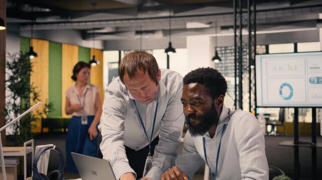 Diverse corporate office scene with team collaboration around laptop and reports, research and development. Professional people analyzing KPI metrics and insights for business intel.