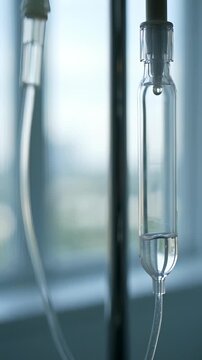 Medical IV drip chamber dropping clear saline solution in a hospital room, symbolizing chemotherapy and hydration therapy.