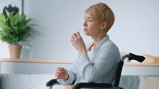 Post-traumatic depression. Unhappy middle aged woman with disability crying, sitting at home in wheelchair, feeling lonely and abandoned, looking at window, slow motion, empty space