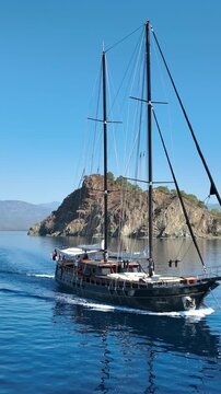 Elegant wooden gulet sailing on a clear blue sea near a rocky coastline