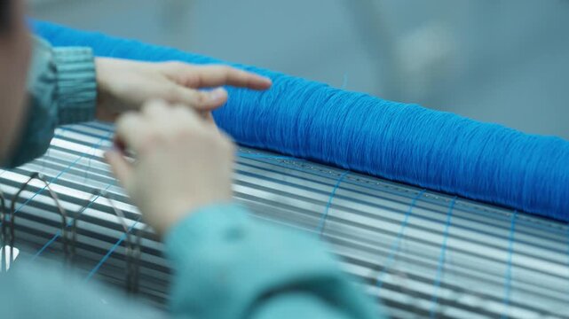 Worker manually operating a blue textile spool in a factory setting