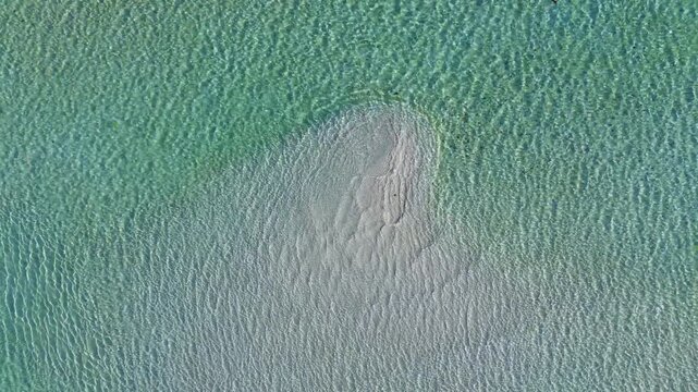 Aerial top-down view of turquoise water looping over a submerged sandbar