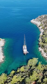 Aerial view of a traditional gulet sailboat anchored in a secluded turquoise bay with rocky shores