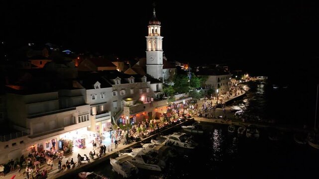 Night view of Sutivan Riva filled with people, illuminated church and festive atmosphere on Brac island, Dalmatia, Croatia.