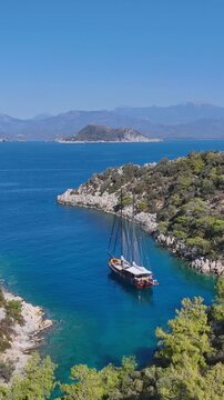 Traditional wooden gulet sailing boat anchored in a secluded turquoise bay with lush green hills