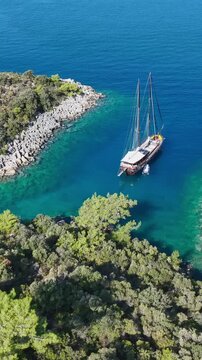 Aerial view of a traditional wooden gulet sailing in a secluded turquoise bay with lush green coastline