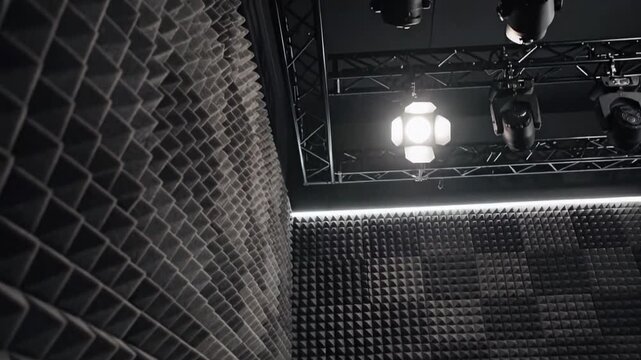 Acoustic foam panels cover studio walls and ceiling, moody low light with rigging and spot lamps, soundproof room for recording podcast voiceover and music rehearsal