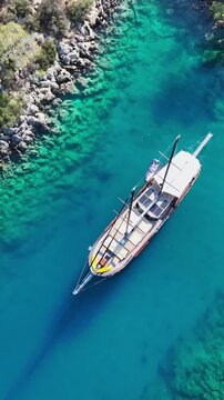 Aerial view of a wooden gulet sailing in crystal clear turquoise Mediterranean waters near rocky coast