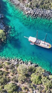 Aerial view of a traditional wooden gulet sailing in a turquoise bay surrounded by rocky shores and lush greenery