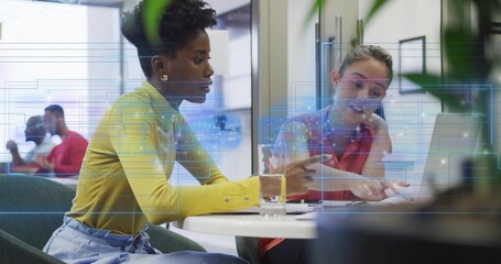 Pointing, two women in yellow, coral working in office at round white table with laptop overlay