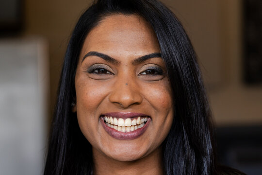Indian woman wearing eye makeup and lipstick smiling broadly at office with blurred background