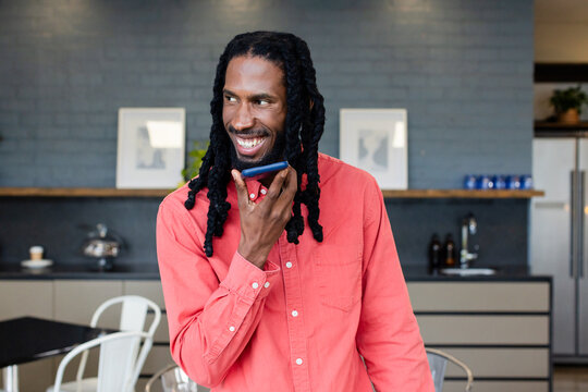 African American male holding smartphone near mouth talking in office kitchenette with coffee cup