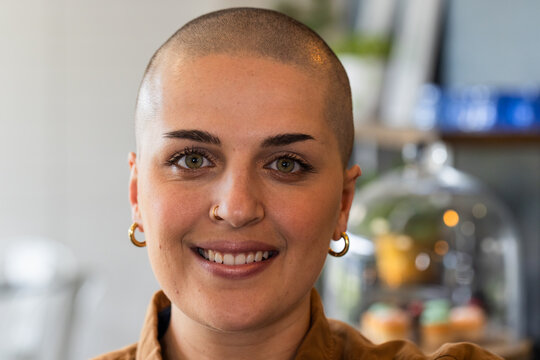 Woman smiling at camera at coffee shop wearing nose ring with pastry display dome in background