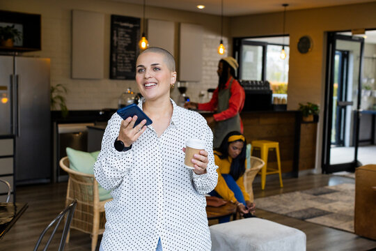 Diverse group at cafe with woman holding cup and smartphone, barista operating espresso machine