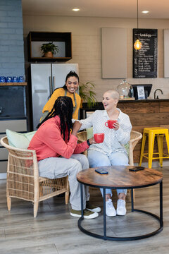Diverse coworkers chatting and sipping coffee with red mugs in lounge by refrigerator, QR code sign