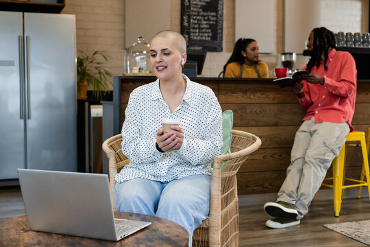 Diverse group sipping coffee and using laptop in cafe beside pastry displays, chalkboard menu