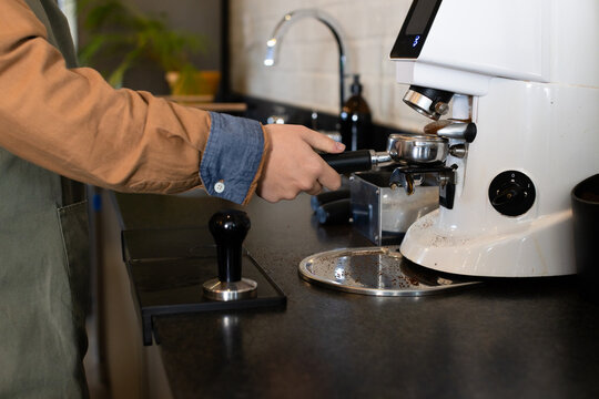 Portafilter catching espresso grounds under grinder spout on black countertop with steel tamper