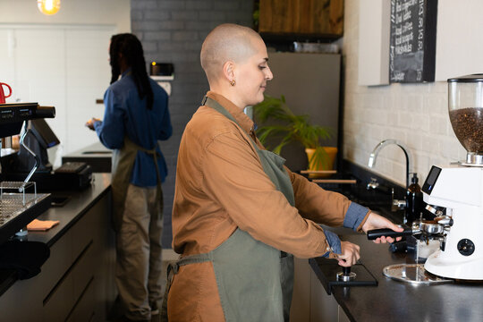 Diverse coworkers operating espresso machine and processing orders behind coffee counter
