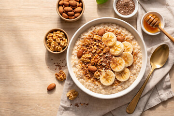 Obraz premium Photorealistic flat lay image of warm oatmeal topped with banana slices, almonds, walnuts, flax seeds, and cinnamon.