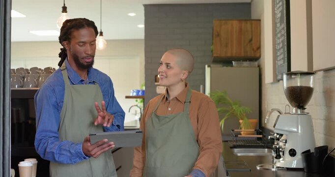 Diverse coworkers at cafe counter pointing at tablet and swiping through orders, smiling at camera