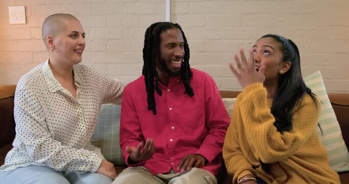 Diverse friends responding to mustard-sweatered woman leaning, laughing and talking on leather sofa