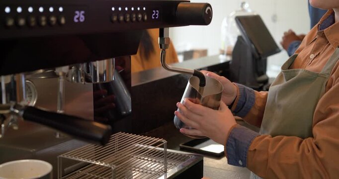 Steam control knob turning, barista steaming milk in stainless pitcher on counter for espresso foam