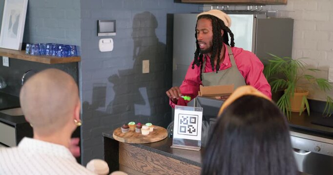African American male barista arranging cupcakes on board after customer pointing serving via tongs