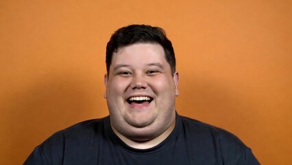 Fototapeta premium Happy caucasian young adult male smiling against orange background.